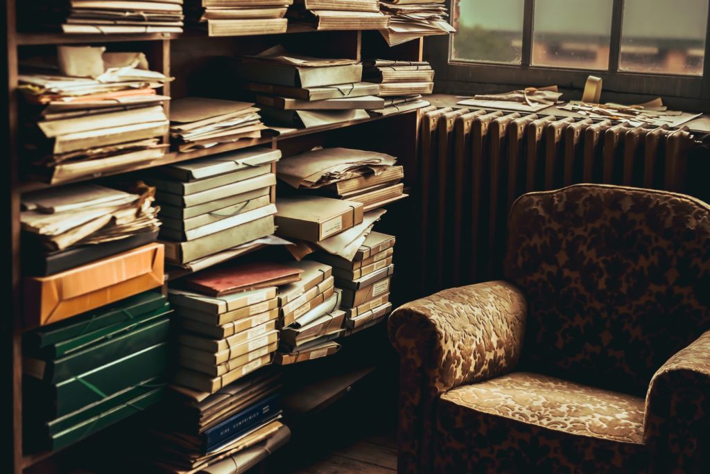 Old armchair near shelves with heap of papers